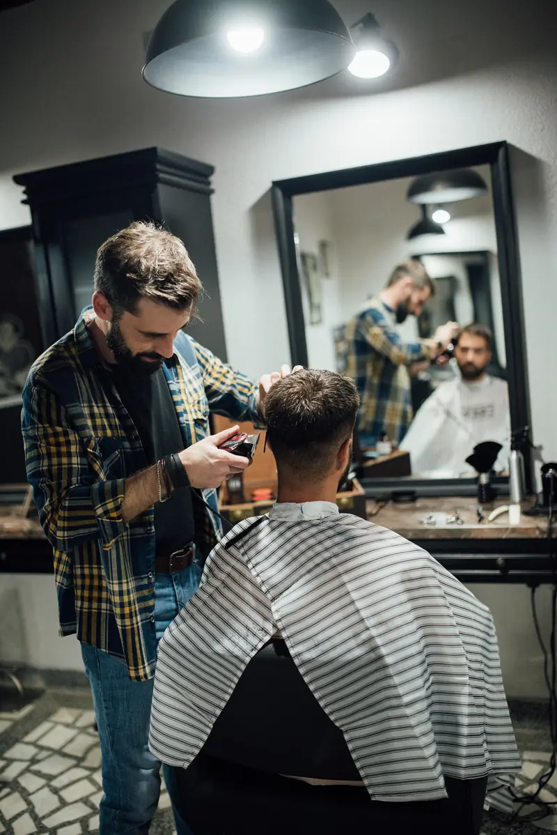 Kapster memotong rambut pelanggan di depan cermin